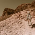 Astronaut in a space suit walking uphill on a rocky, desert-like alien planet.
