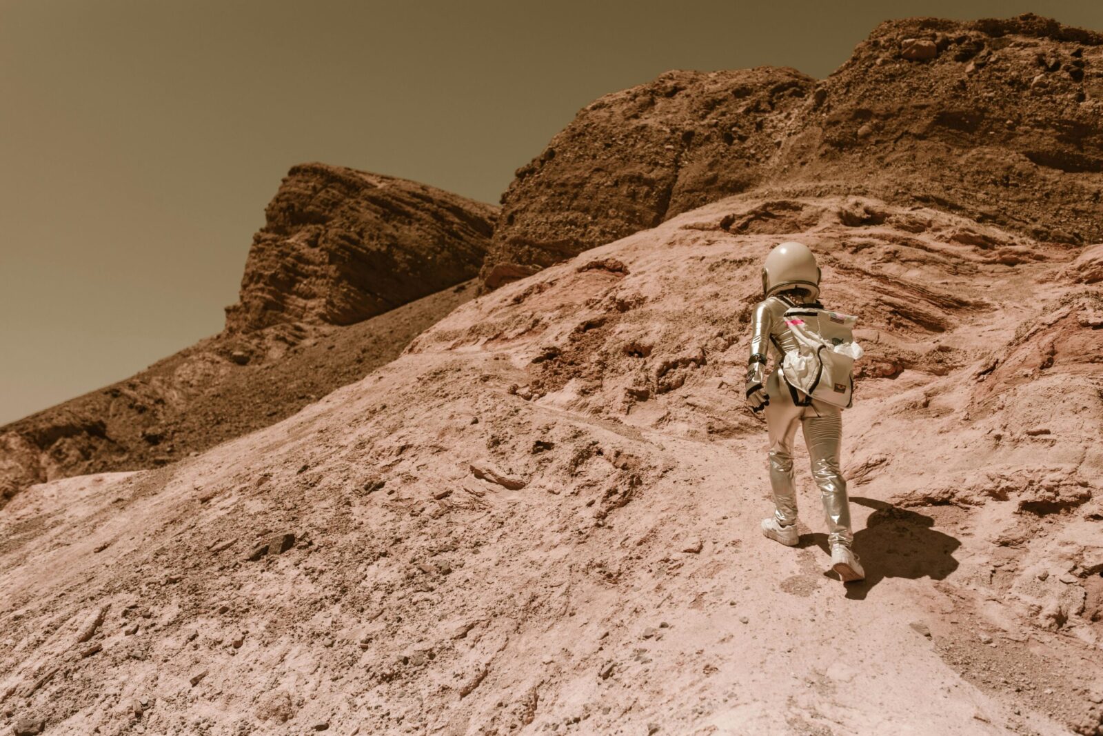 Astronaut in a space suit walking uphill on a rocky, desert-like alien planet.